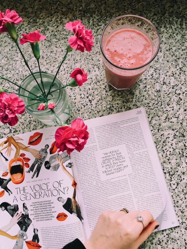 A fresh pink carnation vase, magazine, and smoothie on a speckled countertop.